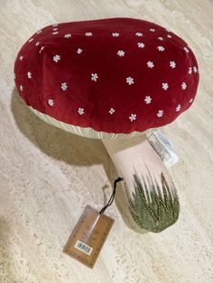 a red mushroom with white flowers on it sitting on the floor next to a tag