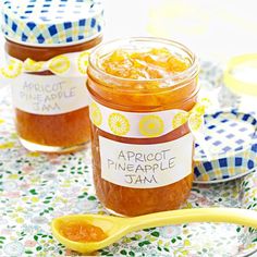 two jars of apricot pineapple jam on a table with a spoon next to them