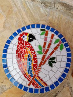 a colorful bird sitting on top of a blue and white mosaic tile wall mounted plaque