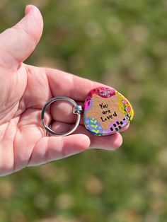 a hand holding a keychain with an image of a cat and the words you loved on it