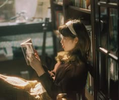 a woman sitting on a chair reading a book in front of a bookshelf