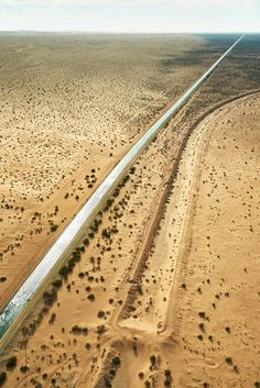 an aerial view of a road in the middle of desert with trees and bushes on both sides