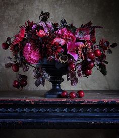 a vase filled with lots of purple flowers and red berries on top of a table