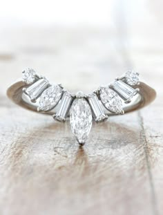 a diamond ring with three pear shaped diamonds on it's side, sitting on a wooden surface