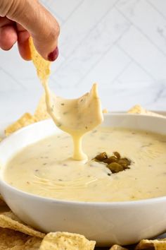 a person dipping tortilla chips into a bowl of quesadilla dip