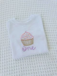 This hand embroidered T-shirt can be customized to your liking, with the name, nickname, or age of your toddler in the stitching font and color you prefer. This high quality, minimalistic design is perfect to slip on your toddler to celebrate their birthday! Hand Embroidered Toddler Shirt, Toddler Birthday Outfit, Cupcake Shirt, Bluey Party, Baby Embroidery, Stitch Shirt, Embroidery On Clothes, First Birthday Outfits, Toddler Birthday