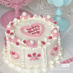 a heart shaped cake with pink icing and white frosting on a table next to lace doily