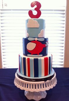 a three tiered cake decorated with blue, red and white stripes on a table in front of a window