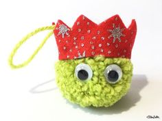 a crocheted green ball with a red crown on it's head and eyes