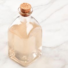 a glass bottle filled with liquid sitting on top of a white marble countertop next to a corked stopper