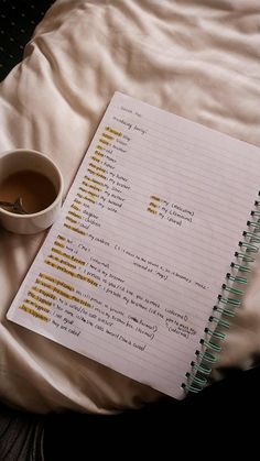 a cup of coffee sitting on top of a bed next to a notebook