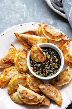 a white plate topped with dumplings and a bowl of dipping sauce next to it