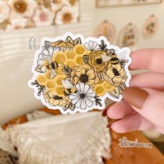 a hand holding up a sticker with bees and flowers on it in front of a bed