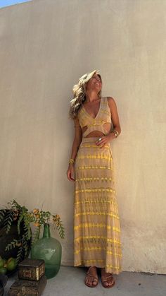 a woman leaning against a wall wearing a yellow dress