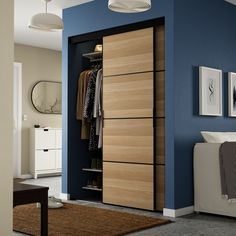 an open closet with clothes hanging on the door and drawers in it, next to a bed