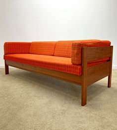 an orange couch sitting on top of a carpeted floor next to a white wall