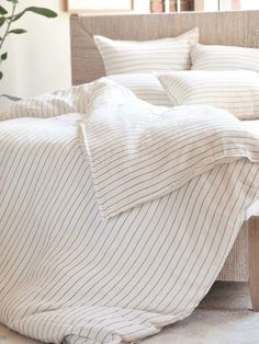 an unmade bed with white and beige striped linens on it, next to a potted plant