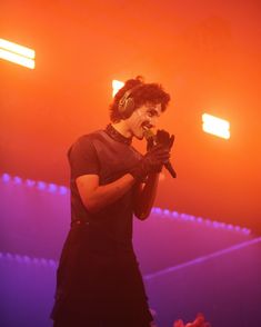 a man with headphones on holding a microphone in front of purple and red lights