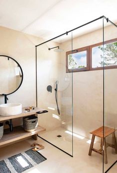 a bathroom with a stand up shower next to a wooden bench and round mirror on the wall