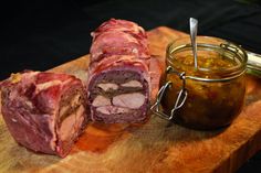 a wooden cutting board topped with meat next to a jar of pickles