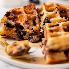 a white plate topped with waffles covered in blueberry sauce next to a fork