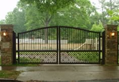 an iron gate with two lights on each side and a stone pillar in the middle