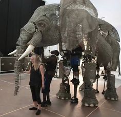 a woman standing next to an elephant statue on top of a hard wood floor in front of a stage