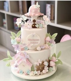 a three tiered cake is decorated with pink and blue flowers, leaves and mushrooms