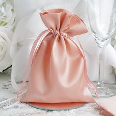 a pink satin bag sitting on top of a table next to two wine glasses and flowers