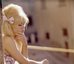 a woman with blonde hair and a bow in her hair is leaning against a pole