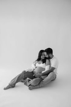 a man and woman sitting on the ground holding each other while they are cuddling