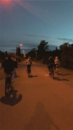 several people riding bikes down a street at night time with the sun setting in the background