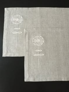 two linen napkins with embroidered flowers on them, one in white and the other in grey