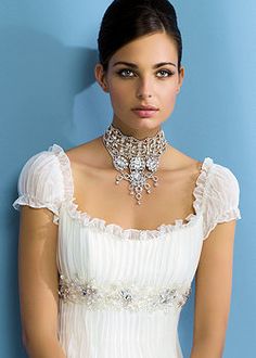 a woman in a white dress with a necklace on her neck standing against a blue wall