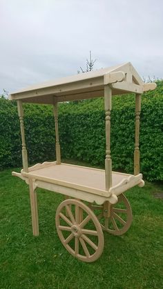 a wooden cart sitting on top of a lush green grass covered field next to a hedge