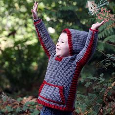 a young boy wearing a crocheted sweater and holding his arms up in the air