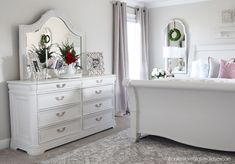 a bedroom with white furniture and christmas wreaths on the dresser next to the bed