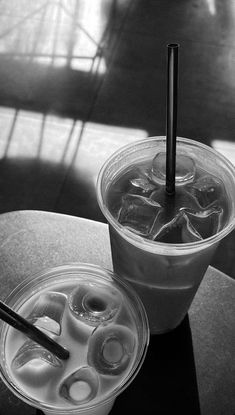 two drinks sitting on top of a table next to each other in plastic cups with lids and spoons