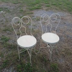 two white metal chairs sitting on top of a grass covered field next to each other