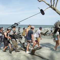 a group of people standing on top of a beach next to the ocean with cameras