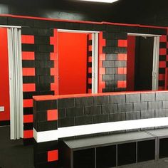 an empty room with red and black tiles on the walls, benches and shelves in front of them