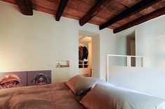 a bed sitting under a wooden ceiling next to a white wall with paintings on it