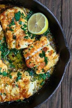 a skillet filled with chicken and vegetables on top of a wooden table next to a lemon wedge