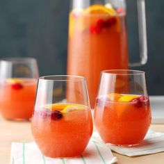 two glasses filled with liquid and oranges on top of a wooden table next to pitcher