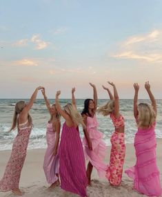 four women in long dresses standing on the beach with their hands up and arms raised