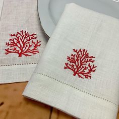 two napkins with red coral designs on them are sitting next to a white plate