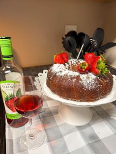 a cake with strawberries on top sitting next to a glass of wine and bottle