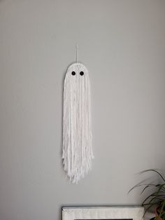 a white wall hanging on the side of a gray wall next to a potted plant