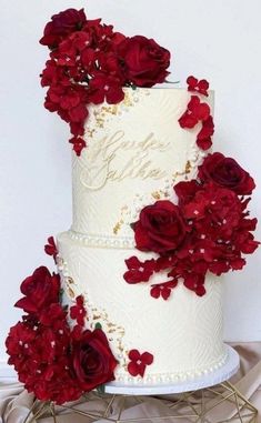 a three tiered wedding cake with red flowers on the side and gold trimmings