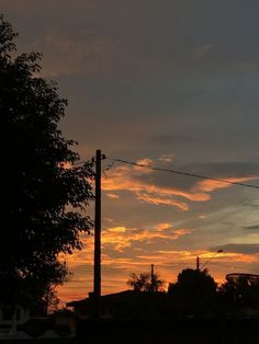 the sun is setting behind some power lines and trees in front of a city street